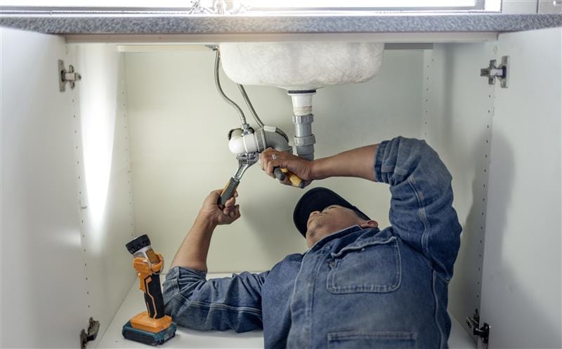 Plumber repairing pipes beneath a bathroom sink in Monrovia